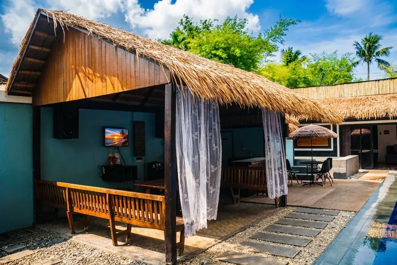 Villa 1 — the thatch-roof videoke cabana viewed from the poolside, TV on the wall and wooden benches under the eaves