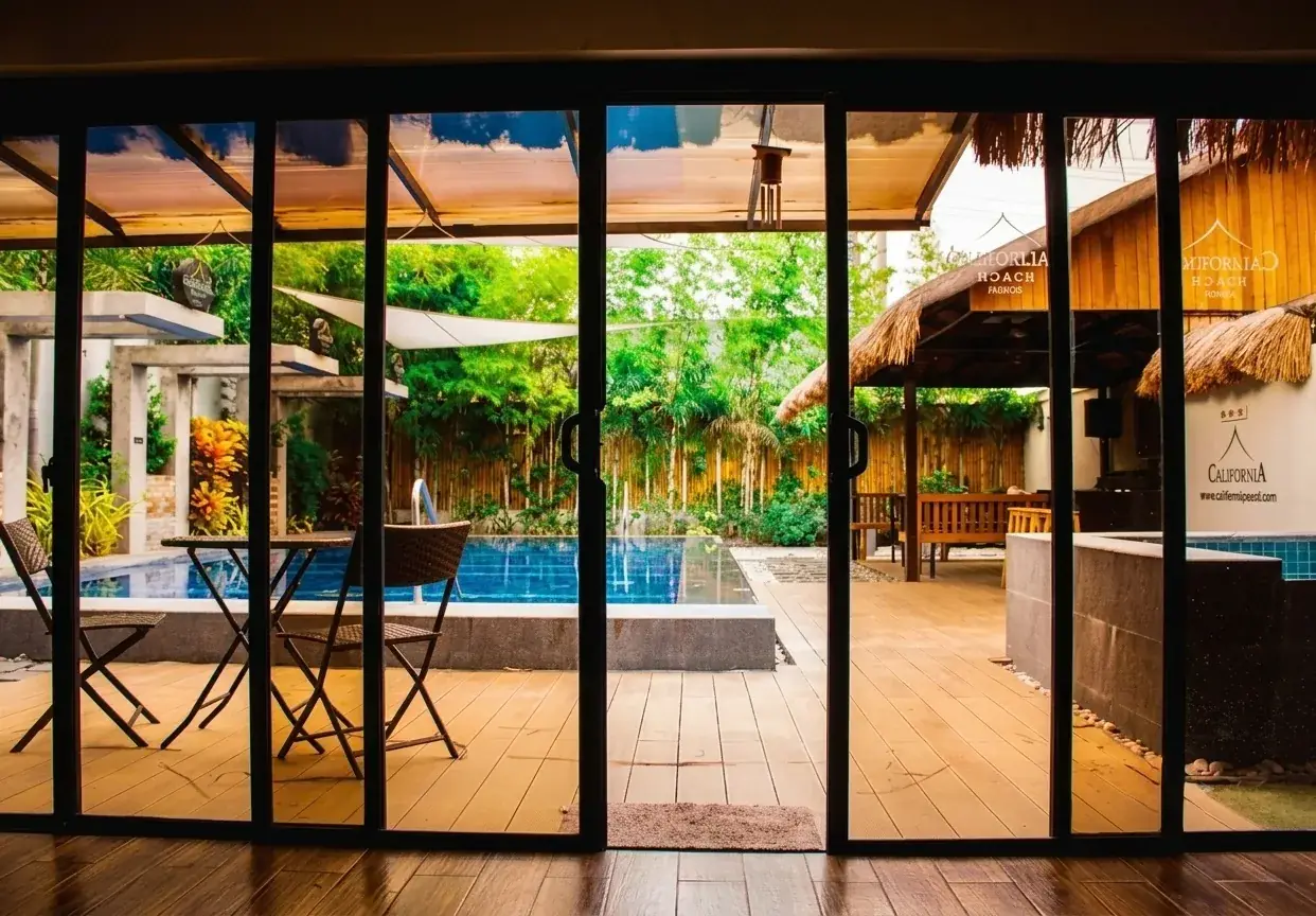 Villa 1 — view from inside the living room through sliding glass doors out to the pool and thatch cabana